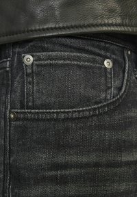 Tamno plavi traperice s detaljnim prikazom prednjeg džepa, vidljivim šavovima i srebrnim detaljima. Tekstura izgleda glatko s blagim sjajem.