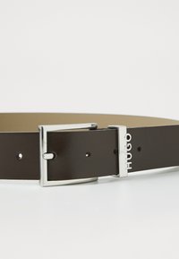 Ceinture en cuir marron avec une texture lisse, dotée d'une boucle en métal argenté gravée du nom de la marque "Hugo."