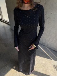 Robe noire à manches longues avec de petits pois blancs, silhouette ajustée et poignets délicats. Tissu lisse avec un léger brillant.