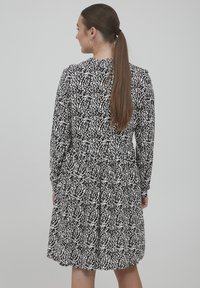 Schwarz-weiß gemustertes Kleid mit langen Ärmeln, einem gerafften Rock und einem hohen Ausschnitt, das ein strukturiertes Stoffdesign aufweist.