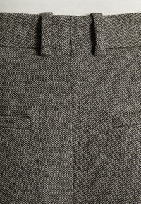 Grijze getextureerde broek met een visgraatmotief, voorzien van dubbele achterzakken en riemlussen bij de taille.