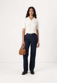 White knitted polo shirt with short sleeves, dark blue straight-leg jeans, and a small textured brown handbag. Black shoes complete the look.