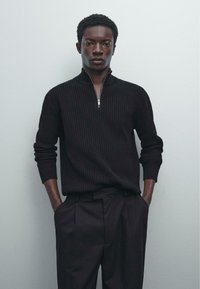 Zwarte geribde trui met een ritssluiting en een neklijn, gecombineerd met zwarte geplaatste broek. Glad textuur, slim fit ontwerp en lange mouwen.