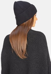 Bonnet noir en tricot côtelé avec un revers, associé à un pull noir texturé, affichant une finition lisse et un design près du corps.