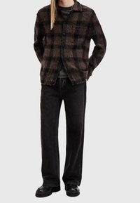 Brun och svart rutigt kofta med knappar, krage och bröstficka, ihop med löst sittande svarta jeans och svarta skor.