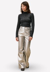 Zwarte, nauwsluitende top met lange mouwen en een gestructureerd patroon; zilveren, wijde broekspijpen met hoge taille; zwart schoeisel met witte accenten.