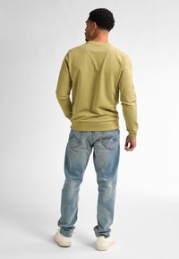 Camisa verde de manga larga con cuello redondo, combinada con jeans de color azul claro y zapatillas de crema. La camisa tiene puños y dobladillo acanalados.