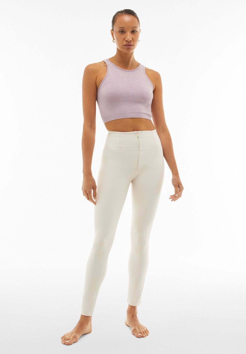 Top corto di colore viola chiaro con texture a coste abbinato a leggings bianchi aderenti a vita alta con dettaglio di zip.