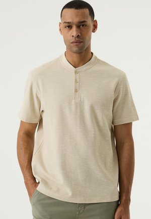 Beige Polohemd mit kurzen Ärmeln aus strukturiertem Stoff, ausgestattet mit einem Stehkragen und einer Knopfleiste mit drei Knöpfen. Lässige Passform mit Seitentaschen.