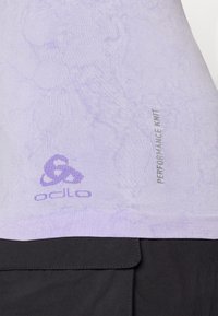 Světle fialové tričko s výkonnostním pletením a texturovaným vzorem, na kterém se nachází logo a štítek "Performance Knit" v kontrastní šedé barvě.