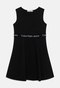 Czarna sukienka bez rękawów z rozkloszowaną spódnicą, z szerokim elastycznym pasem z białym napisem "Calvin Klein Jeans". Gładka faktura.