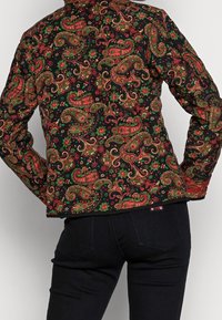 Zwarte jas met een ornamentale paisley-design in rood, groen en goud, met lange mouwen en een getailleerde pasvorm.