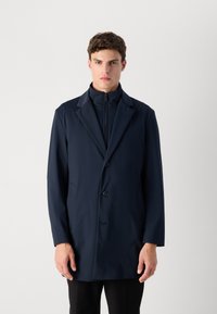 Cappotto impermeabile blu navy con colletto alto, chiusura a singolo bottone e design minimalista. Texture liscia e senza motivi o accenti visibili.