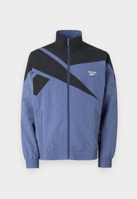 Reebok windbreaker jacket in blue and black, featuring angular graphic design, zip front, elastic cuffs, and side pockets.