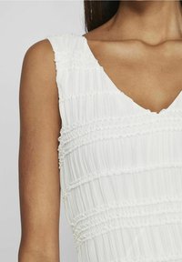 Vit ärmlös klänning med V-ringning, texturerad och plisserad yta samt samlade horisontella ränder över tyget.