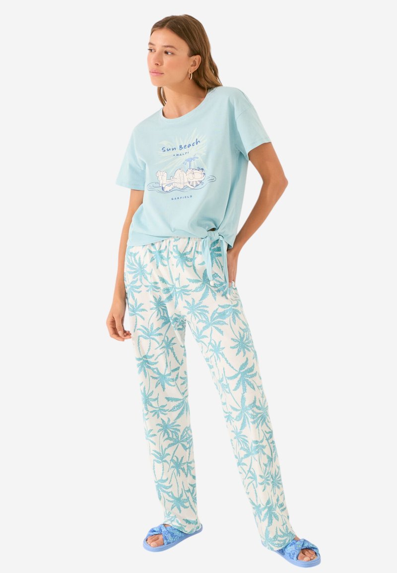 T-shirt en coton bleu clair avec impression graphique ; pantalon de lounge à motifs de palmiers en blanc et aqua ; sandales en bleu. Conception à coupe décontractée.