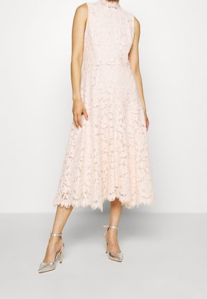 Ärmelloses, blassrosa Spitzen-Midikleid mit hohem Ausschnitt, Blumenmuster und gewelltem Saum, getragen mit silbernen High Heels mit Knöchelriemen.