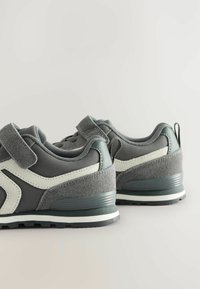 Ein Paar graue und weiße Kindersneaker mit Klettverschlüssen, strukturierten Sohlen und Ziehschlaufen auf einem hellen Hintergrund.