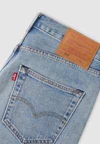 Φωτεινά γαλάζια τζιν από τζην ύφασμα με δερμάτινο ταμπελάκι που αναγράφει «Levi Strauss & Co.» και χαρακτηριστική πίσω τσέπη με ραμμένες καμάρες.