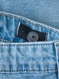 Tela de mezclilla azul claro con una cinturilla azul oscura y un botón de presión gris. Presenta costuras visibles y variaciones de textura.