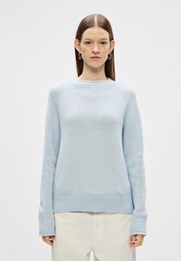 Světle modrý pletený svetr s kulatým výstřihem, žebrovanými manžetami a spodním lemem a měkkou texturou. Volný střih s raglánovými rukávy.