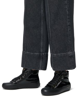 Baskets montantes noires en cuir verni, avec des lacets à l'avant, des accents texturés et une semelle en caoutchouc, associées à un pantalon large noir.