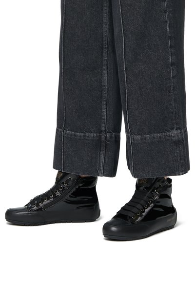 Black high-top sneakers made from glossy patent leather, featuring lace-up fronts, textured accents, and a rubber sole, paired with wide black pants.