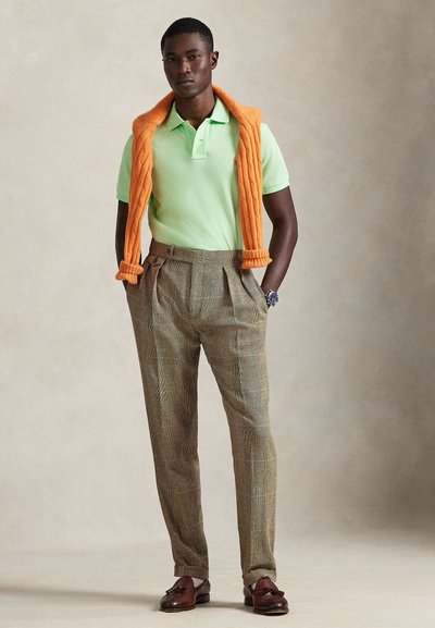 Πράσινο πόλο πουκάμισο, πορτοκαλί πλεκτό πουλόβερ περασμένο πάνω από τους ώμους, καρό παντελόνι σε καφέ αποχρώσεις και σκουρόχρωμα καφέ μοκασίνια. Λεπτό ύφασμα, εφαρμοστή ραφή.