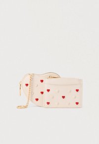 Portefeuille beige compact orné de motifs en forme de cœur rouges et crème. Il possède une fermeture éclair et une chaîne dorée pour un transport facile.