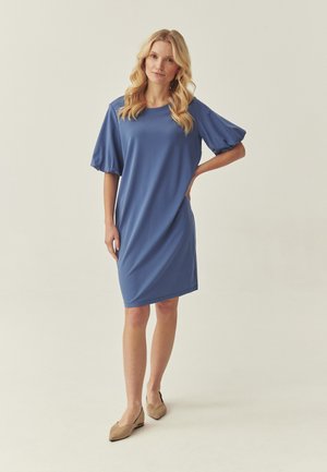 Blå knælængde kjole med korte, puffede ærmer. Glat stof med en afslappet pasform. Bruges med lyse beige flade sko på en neutral baggrund.