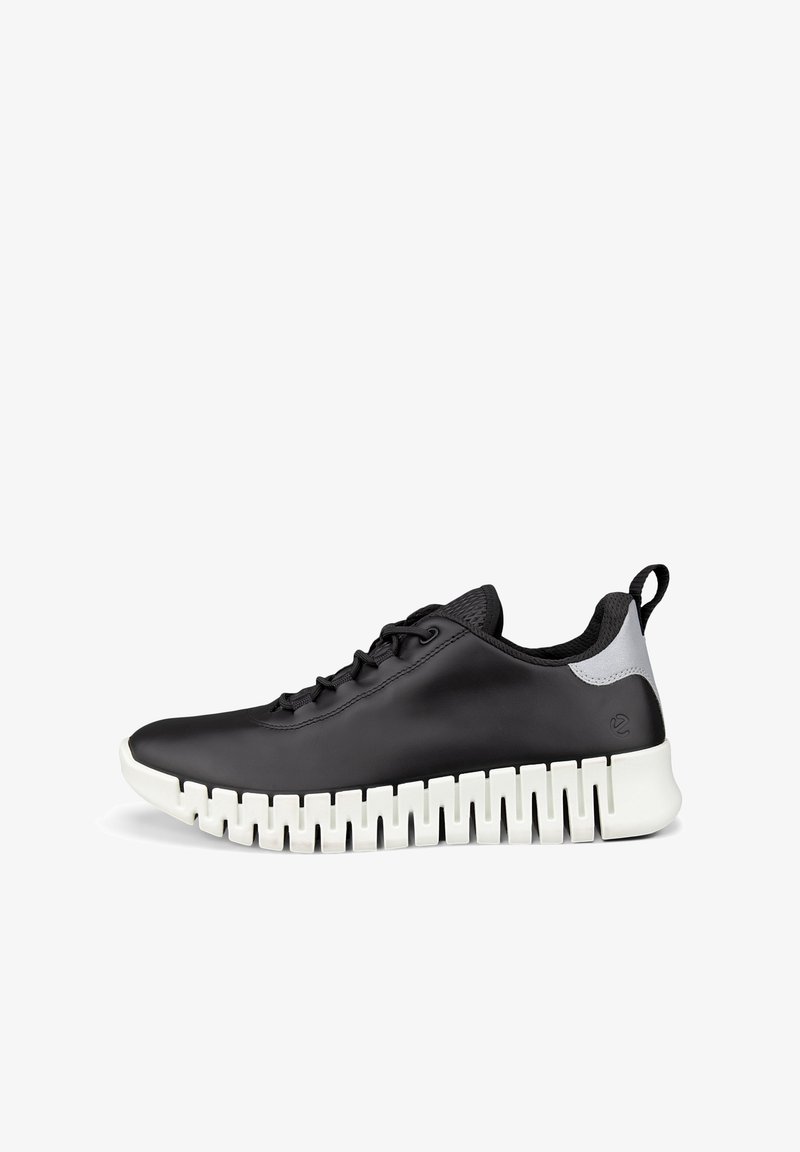 Chaussure de sport noire avec semelle blanche segmentée, lacets noirs, col rembourré et languette au talon.