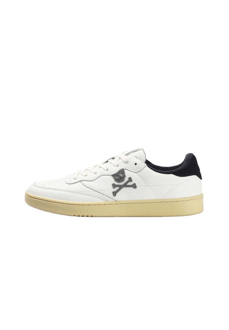 Zapatilla blanca con acentos negros, material de cuero suave, punta redonda, diseño con cordones y un logo de calavera y tibias cruzadas en el lateral.