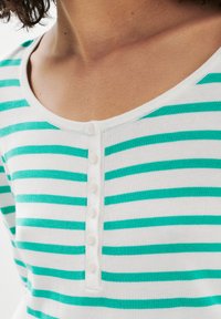 T-shirt rayé blanc et turquoise avec un col rond et une patte de boutonnage, fabriqué en un tissu en maille doux et léger.