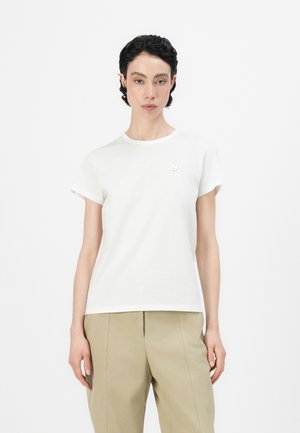T-shirt bianco in cotone con scollatura rotonda, maniche corte e un piccolo accento ricamato sul petto. Texture morbida e vestibilità classica.