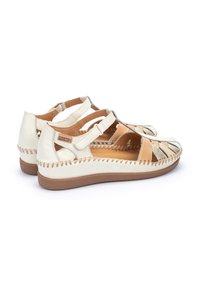 Sandalias de cuero en color blanco roto con diseño cortado, correa ajustable y acentos cosidos. Cuenta con una plantilla acolchada y suela plana.