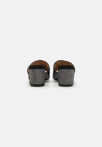 Chaussures noires avec un dessus texturé, ornées de embellissements en strass métalliques. Les talons sont solides, arrondis et relativement bas.