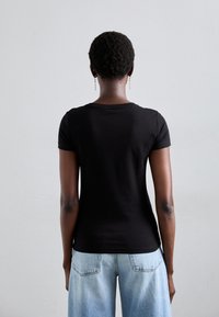 Zwarte, korte mouwen t-shirt van glad katoen. Beschikt over een klassieke ronde halslijn en een iets aangesloten vorm. Draagt met lichtblauwe jeans.