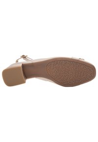 Scarpa con tacco beige con suola testurizzata e decorata. La tomaia presenta un materiale liscio e una cintura con fibbia per la chiusura.