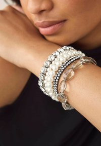 Clear and textured bracelets: one with faux pearls, one with silver accents, one with clear faceted beads, layered on a wrist.