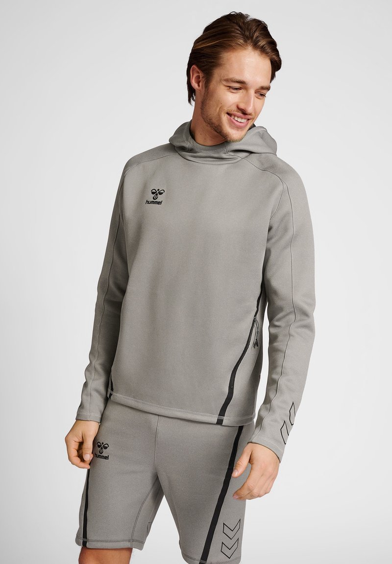 Haut de survêtement en gris avec capuche, manches longues, accents noirs et poche zippée. Associé à un short assorti avec un design rayé et un logo.