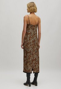 Maxi jurk met luipaardprint en dunne bandjes, gemaakt van zacht materiaal. Heeft een split aan de achterkant en een zwarte zoom, gecombineerd met kniehoge zwarte laarzen.