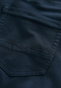 Tessuto blu navy scuro con una texture liscia presenta una tasca posteriore con cuciture angolari e una sottile lucentezza, che ne evidenzia il design sartoriale.