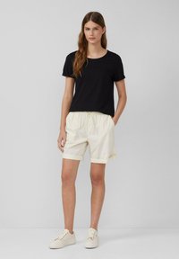 T-shirt noir à manches courtes associé à un short crème à taille élastique, avec des manches retroussées et des baskets de couleur claire. Design simple et fonctionnel.
