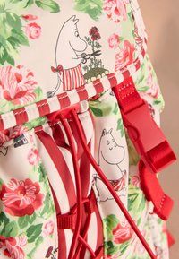 Kleurrijke stoffen rugzak met bloemenpatronen in roze en groen, met rode banden en details. Opvallend ontwerp met een cartoonfiguur.