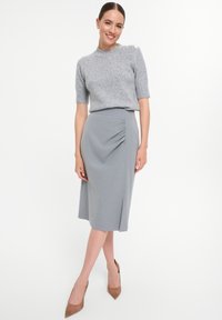 Grau strukturierter Pullover mit kurzen Ärmeln und dekorativen Knöpfen an der Schulter, kombiniert mit einem Bleistiftrock mit seitlicher Raffung und Schlitz.