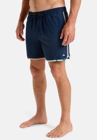 Bañador navy con cinturilla elástica y cordón. Presenta rayas de acento multicolores en el dobladillo y un detalle de logo en el costado.