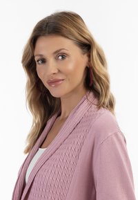 Lys pink cardigan med ribbet tekstur og sjalkrave. Modellen bærer burgunder hoops og en hvid top under.