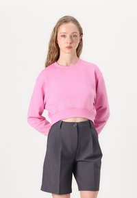 Rosa Cropped sweatshirt med lange ermer og rillet mansjetter, parret med mørkegrå skreddersydde shorts med frontknapp og folder.