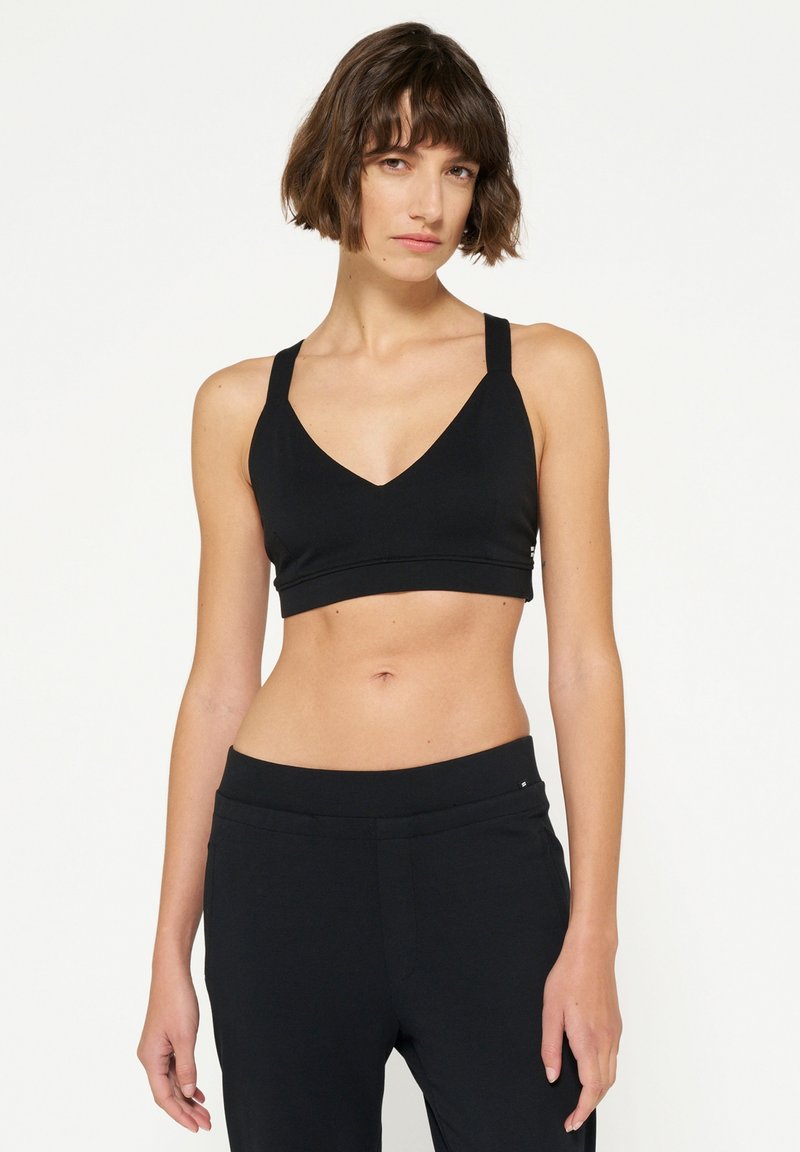 Sujetador deportivo negro con un diseño de escote en V, tirantes anchos y una banda sin costuras. Textura suave, estilo minimalista, combina con pantalones negros.