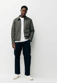 Szürke szövetkabát gallérral, fehér póló alatt, sötétkék nadrággal és fehér tornacipővel párosítva. Egyszerű, letisztult kialakítás.